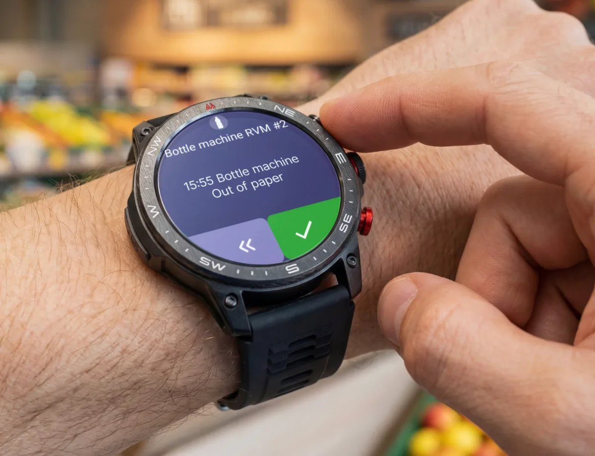 Close-up of a cWatch smartwatch showing a proactive alert that a bottle return machine is out of paper